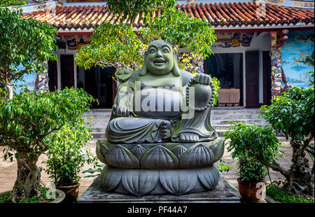 Un grande Buddha di grasso con piccole piante e alberi di fronte a un tempio, una popolare attrazione turistica a sud di tonalità, Vietnam. Foto Stock