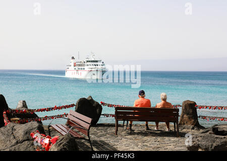 LANZAROTE, Spagna - 18 Aprile 2018: coppia di turisti senior seduta su una panchina in cerca di una grande nave proveniente su Playa Blanca Harbour, Lanzarote, Canarie Foto Stock