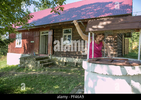 Teodorówka, Polonia - Agosto 14, 2017: Una donna sta prendendo l'acqua dal vecchio, pietra, acqua bene con un verricello a manovella e nel villaggio polacco. In Foto Stock