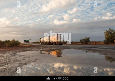 Un australiano Road Train con 3 rimorchio passando da e riflettendo in una pozzanghera. Con lanosa nuvole e luce dorata Foto Stock