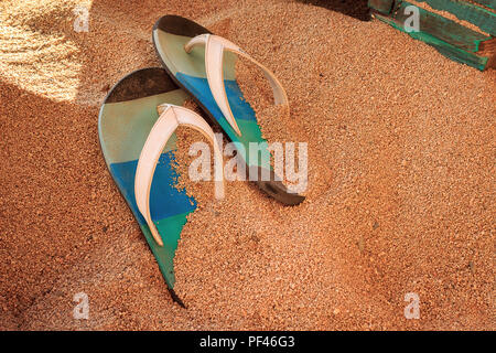 Colorato flip-flop su un golden, sabbia fine su una spiaggia in un bar con mobili in legno Foto Stock