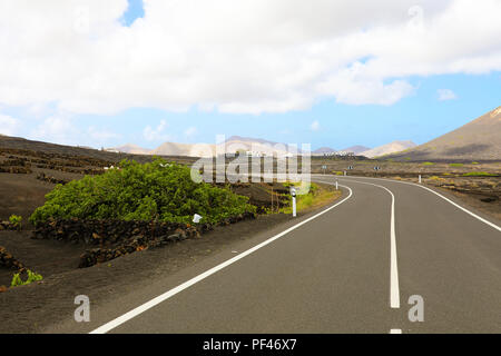 Alla guida di una vettura a Lanzarote Island road. Strada asfaltata curvi tra i vigneti con terra nera e vulcani sullo sfondo. Bella strada con na Foto Stock