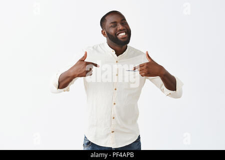 Io sono migliori. Ritratto di bell'aspetto fiducioso e contento americano africano barbuto ragazzo con brevissimo scarto, puntando verso di sé con orgogliosa e felice espressione, in piedi su sfondo grigio Foto Stock