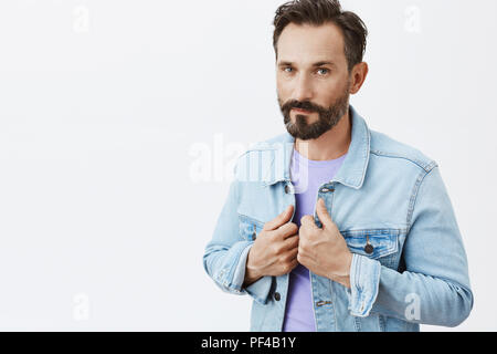 Pronto colpito e conquistare. Ritratto di bella ed elegante fiducioso imprenditore maschio in denim camicia al di sopra t-shirt viola, toccando il collare e fissando con auto-espressione garantita in telecamera Foto Stock