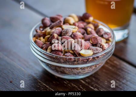 Piccola Coppa in vetro con arachidi salate e bicchiere di birra in background Foto Stock