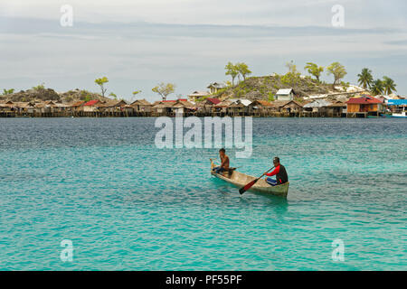 Vista di due uomini pagaiando su una barca tradizionale nella parte anteriore del bajo villaggio con case di legno sulle isole Togean nelle Sulawesi, Indonesia Foto Stock