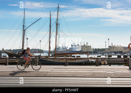 Finlandia ciclismo estate, la vista di una donna in bicicletta lungo il fronte del porto della città di Helsinki su una mattina d'estate, Finlandia. Foto Stock