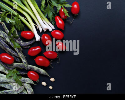 Ortaggi freschi pomodori, cipollotti, prezzemolo, non cotti fagiolini giacciono su uno sfondo scuro close-up vista da sopra Foto Stock