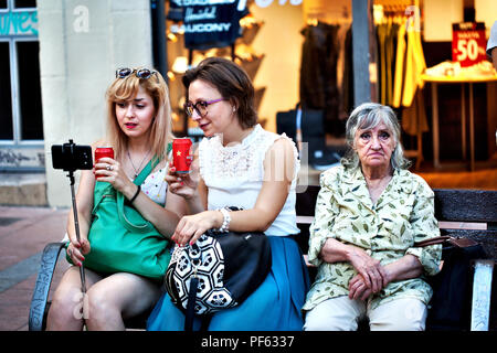 Una donna locale seduto su una panchina accanto a due turisti guardando le foto su uno smartphone. Foto Stock