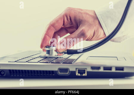 L'uomo controllando il suo computer portatile con uno stetoscopio tenendo premuto il disco oltre la tastiera come egli cerca di virus e malware, tonico o retrò instagram e Foto Stock
