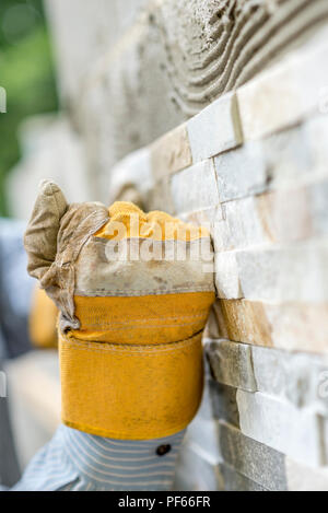 Primo piano della parte maschio in protezione guanto di lavoro rendendo un pugno durante la pressatura di una piastrella ornamentali in una colla per fissarlo su una parete. Foto Stock