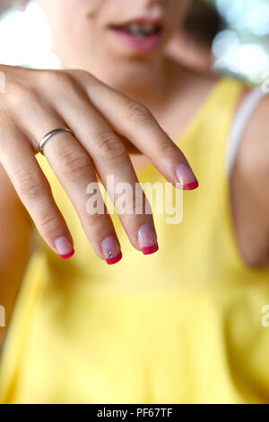 Primo piano della mano femminile con belle french manicure indossare anello di fidanzamento in oro bianco. Foto Stock