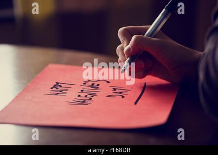 Primo piano della femmina di scrittura a mano felice il giorno di San Valentino la frase su carta rossa sul tavolo di legno, effetto retrò aspetto sbiadito. Foto Stock