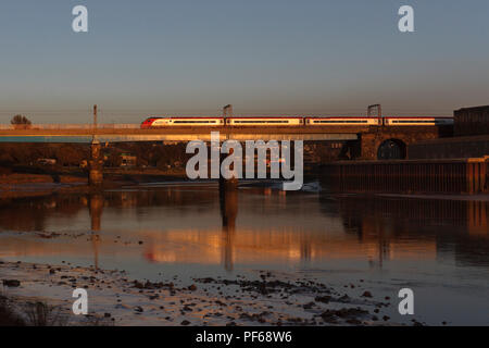 Treni del Virgin Pendolino 390054 attraversando il ponte di Carlisle, Lancaster (fiume Lune) glinting al tramonto e riflessa nel fiume Foto Stock