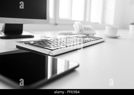 Compressa vuota, la tastiera e il computer desktop su un bianco scrivania o tavolo di office in un basso angolo di visione con riflessi sullo schermo. Foto Stock