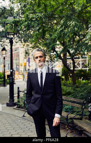 Capelli grigi Man in Black Suit le passeggiate attraverso un parco Foto Stock