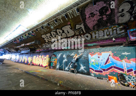 Un artista la spruzzatura di vernice sul muro in un tunnel in London, London, England, Regno Unito Foto Stock