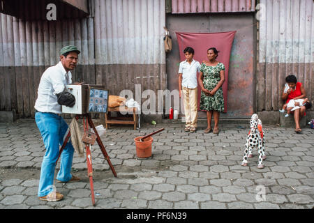 Managua, Nicaragua, luglio 1986; Astreet fotografo fa un ritratto di una madre e suo figlio, usando la fotocamera per sviluppare la stampa finale. Foto Stock