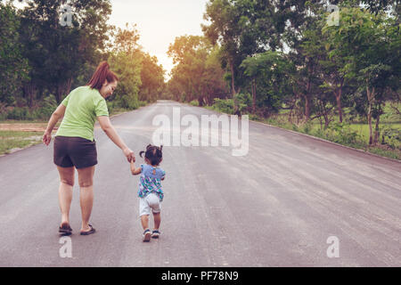 Madre tenendo una mano di sua figlia a camminare nel parco pubblico Foto Stock