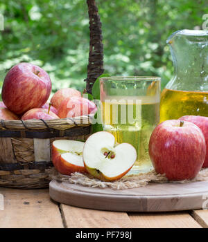 All'aperto con un bicchiere e brocca di succo di mela e fresche Mele rosse su rustico superficie in legno Foto Stock