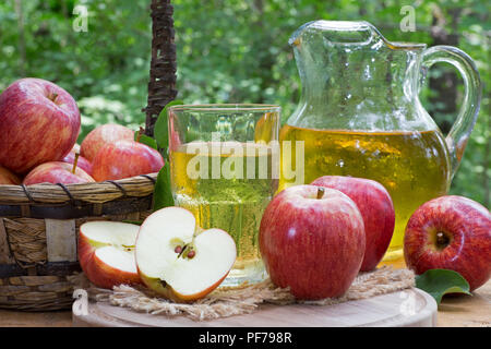 All'aperto con un bicchiere e brocca di succo di mela e fresche Mele rosse su rustico superficie in legno Foto Stock