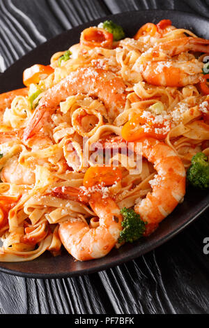 Ricetta italiana pasta fettuccine con gamberi, calamari, broccoli, formaggio con salsa di pomodoro closeup su di una piastra verticale. Foto Stock