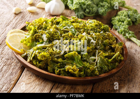 Cavolo verde o una foglia di cavolo cotto con cipolle, aglio, olio di oliva e limone close-up su una piastra su un piano orizzontale. Foto Stock
