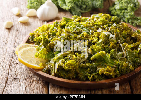 Foglie di cavolo stufato con cipolle, aglio, olio di oliva e limone close-up su una piastra e gli ingredienti sul tavolo orizzontale. Foto Stock