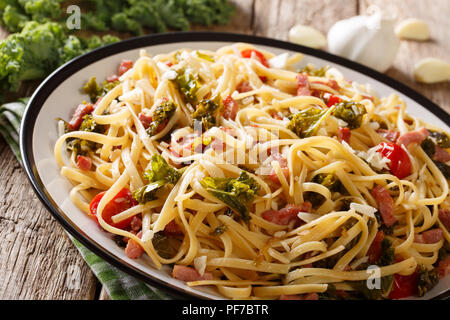 Pasta fatta in casa con kale fritte, pancetta, pomodori, aglio e parmigiano close-up su una piastra orizzontale. Foto Stock