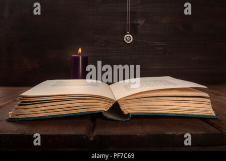 Una foto di un vecchio libro su sfondo scuro con una candela che brucia, un pentacle, e spazio di copia Foto Stock