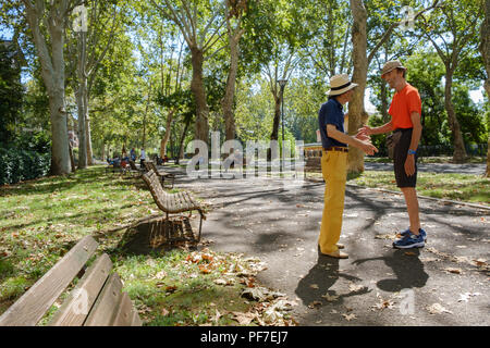 Vestiti in maniera colorata gli uomini italiani sia con cappelli di paglia per incontrare e salutare ogni altro su una mattina estati al parco. Piacenza, Italia. Foto Stock