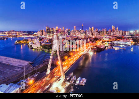 Cavo luminoso Anzac ponte sul porto di Sydney che conduce al CBD della città illuminata al tramonto sotto il cielo blu scuro in Australia. Foto Stock