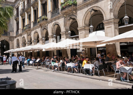 La gente seduta sotto grandi ombrelloni aventi il cibo e le bevande lungo il cortile della Plaça Reial square, Barcellona, Spagna Foto Stock