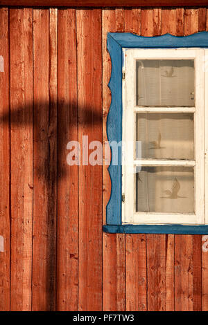 Ombra da un lampione su una tavola di legno parete dipinta con una finestra bianca e tende di pizzo in una giornata di sole Foto Stock