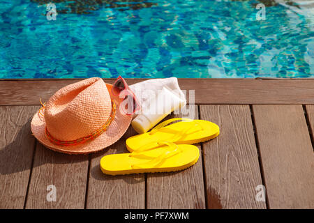 Cappello, occhiali da sole e protezione solare a lato della piscina, in estate il concetto di viaggio Foto Stock