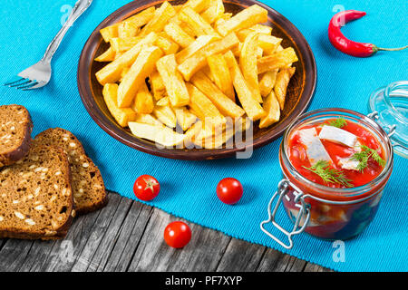 Patate fritte con pezzi di peperoncino sul piatto bianco e fette di marinato aringa norvegese in salsa di pomodoro in pezzi di pane di segale, il g Foto Stock