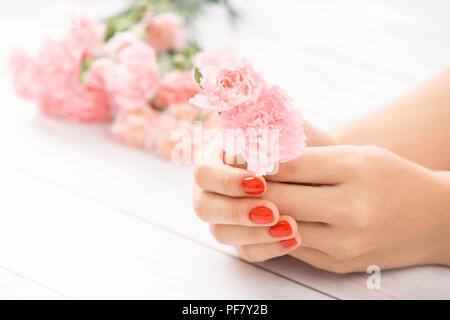 Mani femminili con red manicure e una bottiglia aperta di vernice sul tavolo Foto Stock