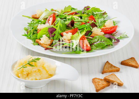 Insalata fresca di pomodori ciliegia,crostini e capelin roe, misti foglie di lattuga nel piatto bianco sul vecchio tavolo in legno, vista dall'alto Foto Stock