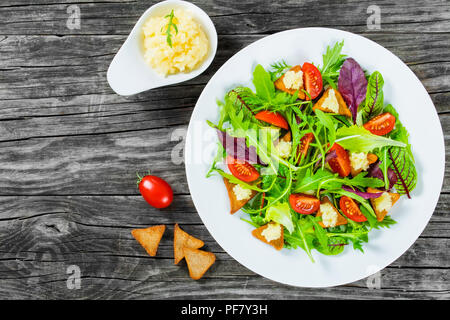 Insalata fresca di pomodori ciliegia,crostini e capelin roe, misti foglie di lattuga nel piatto bianco sul vecchio tavolo in legno, vista dall'alto Foto Stock