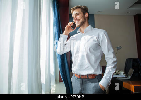 Caucasica adulto medio imprenditore parlando con un telefono mobile in camera in hotel durante il viaggio di affari. Foto Stock