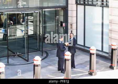London, Regno Unito - 22 Giugno 2018: due imprenditori, uomini che indossano abiti, in piedi di fronte a office corporate, edificio commerciale ingresso nel centro cittadino Foto Stock