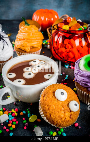 Divertente per bambini tratta per la festa di Halloween, creepy la cioccolata calda con marshmallow occhi e divertente monster tortini, su sfondo blu scuro con canditi, Foto Stock