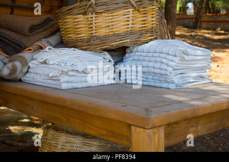 Asciugamani da bagno e coperta di colori diversi nel cesto di vimini sul tavolo di legno in giardino Foto Stock