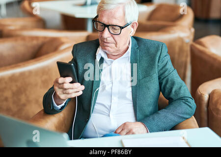 Senior contemporaneo uomo utilizza lo smartphone in Cafe Foto Stock