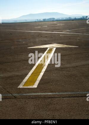 Scatto verticale ad angolo alto di una freccia dipinta di giallo a terra che punta dritto in avanti. Asfalto di un aeroporto. Foto Stock