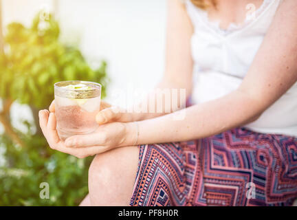 Donna bionda rilassante sul patio holding bevanda ghiacciata Foto Stock