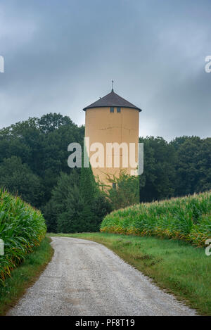 Immagine rustico con un paese di attraversamento stradale tra il verde dei campi di grano e conduce verso una vecchia torre e una foresta, vicino Schwabisch Hall, Germania. Foto Stock