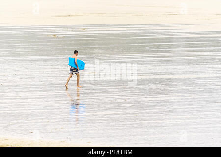 Un vacanziere che porta un corpo boogie board in tutta Fistral Beach in Cornovaglia. Foto Stock