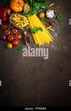 Il cibo italiano sfondo. Pasta non cotta al pomodoro e basilico. Ingredienti per la cottura. Foto Stock