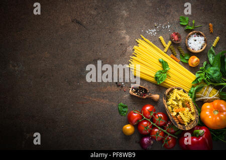 Il cibo italiano sfondo. Pasta non cotta al pomodoro e basilico. Ingredienti per la cottura. Foto Stock